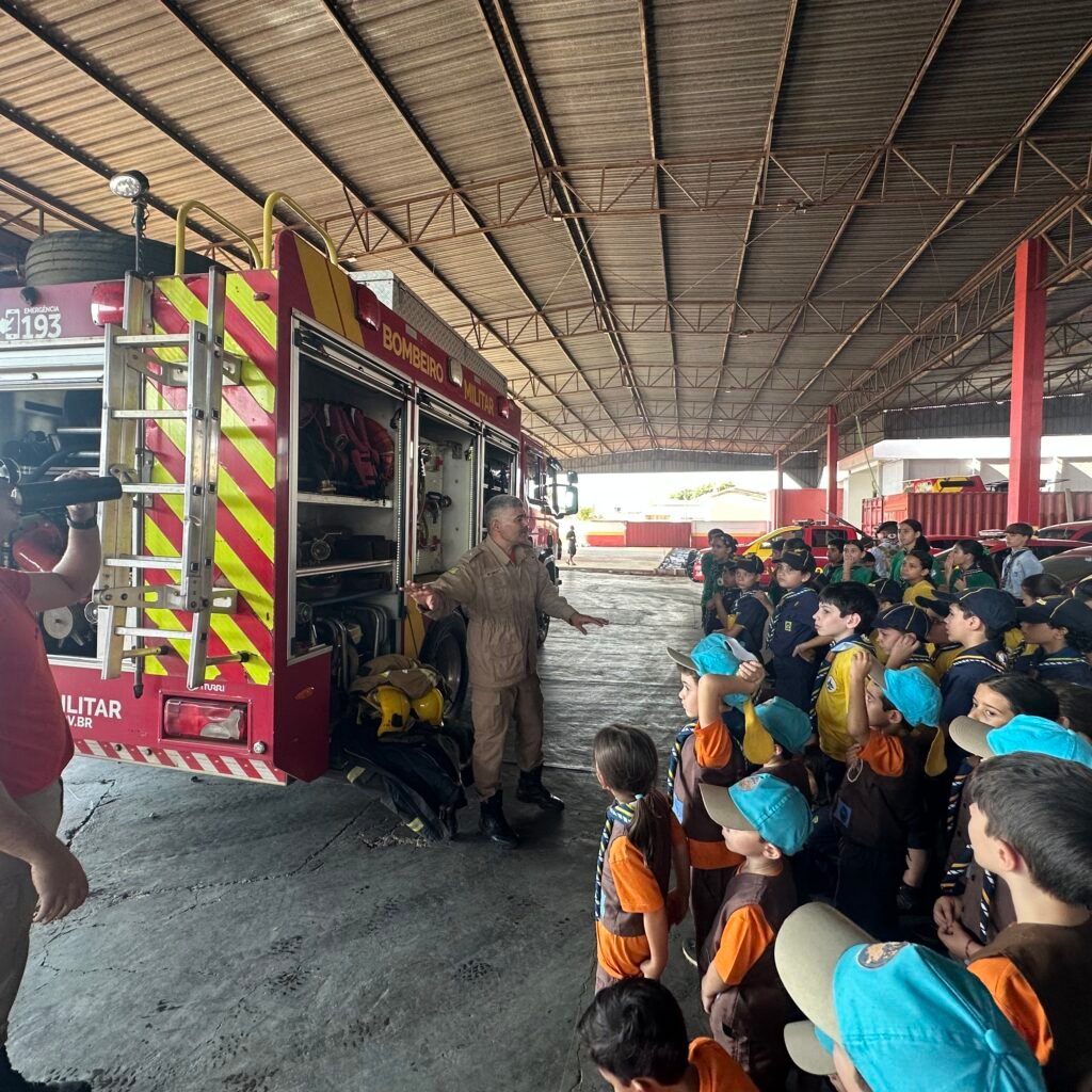 Crianças e jovens do Grupo Escoteiro do Ar Santo Antônio conhecem equipamentos apresentados por bombeiro durante visita ao 3º Batalhão Bombeiro Militar de Anápolis.