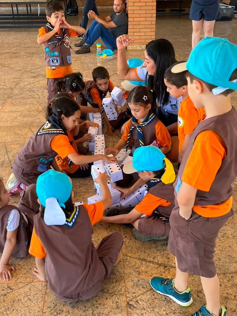 Castores da Colônia Herói Construtor montando uma estrutura com peças de dominó gigante feitas de materiais recicláveis durante o DIQUE Descentralizado 2026.